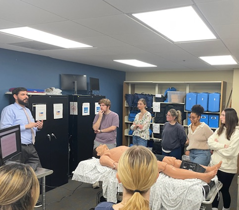 Students listen to an instructor as they stand around a manikin in the SimLab.