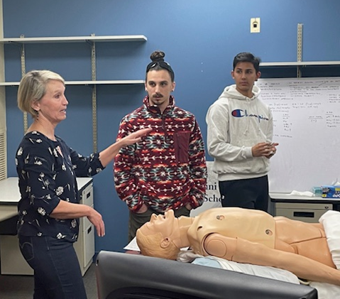 Students listen to an instructor as they stand around a manikin in the SimLab.